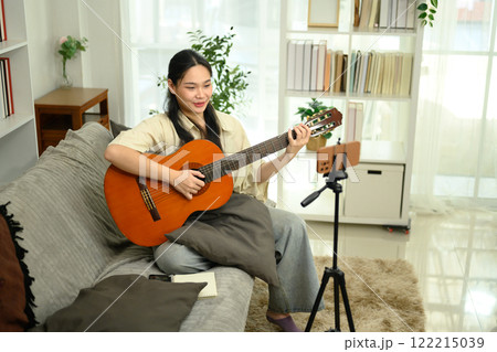 Attractive young woman playing guitar while recording content for social media. Attractive young woman playing guitar while recording content for social media. 122215039