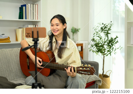 Pretty young artist teaching guitar online recording her lesson with smartphone at home Pretty young artist teaching guitar online recording her lesson with smartphone at home 122215100
