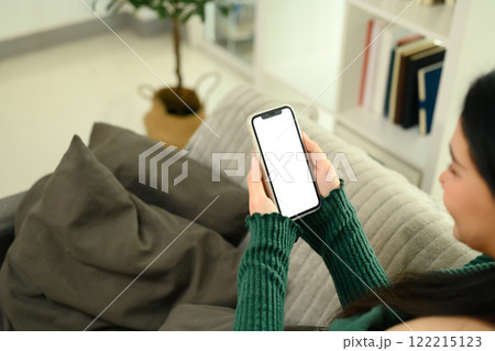 Close up of young woman sitting on a couch holding a smartphone with a blank white screen Close up of young woman sitting on a couch holding a smartphone with a blank white screen 122215123