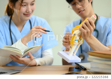 Medical students in scrubs studying anatomy with joint model on the desk Medical students in scrubs studying anatomy with joint model on the desk 122215168