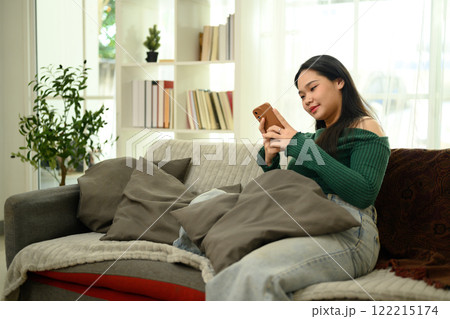Relaxed young woman in sweater and jeans using smartphone on a cozy sofa 122215174