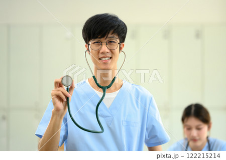 Confident medical student in blue scrubs holding up stethoscope, ready to practice patient care Confident medical student in blue scrubs holding up stethoscope, ready to practice patient care 122215214
