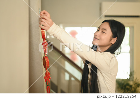 Cheerful asian girl decorating home with red ornaments during Chinese New Year celebration Cheerful asian girl decorating home with red ornaments during Chinese New Year celebration 122215254