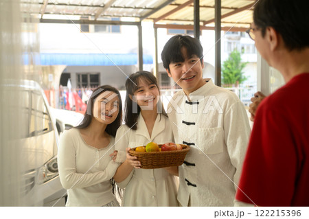 Cheerful family arriving at a relative home during Chinese New Year, carrying a basket of fruits as a gift 122215396