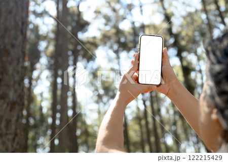 Hands holding smartphone with blank screen in a wooded area and sunlight streaming through the trees 122215429