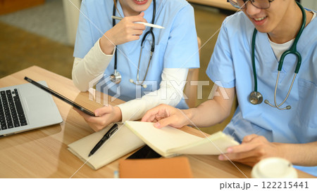 Medical students in blue scrubs reviewing a notes and using digital tablet during study session Medical students in blue scrubs reviewing a notes and using digital tablet during study session 122215441