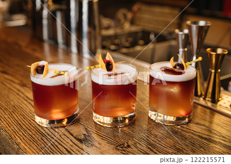 Three vibrant cocktails on a wooden bar counter, perfect for nightlife and mixology themes 122215571