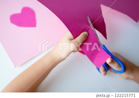 Child crafting. Hands cutting pink paper with scissors for heart art project 122215771