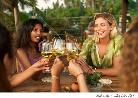 Diverse women cheers with wine glasses in outdoor restaurant. Friends gather, celebrate and connect. Smiles and laughter. Inspired by women club meeting and International Women Day themes. 122216357