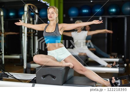 Young woman sitting on box set equipment reformer performs for abdominal muscles Young woman sitting on box set equipment reformer performs for abdominal muscles 122218393