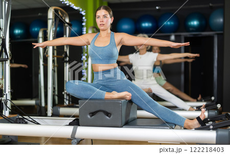 Young woman sitting on box set equipment reformer performs for abdominal muscles 122218403
