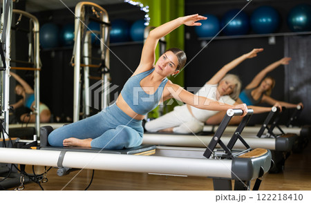 Girl sitting on foldable bed reformer performs exercises, strengthening body and muscles 122218410