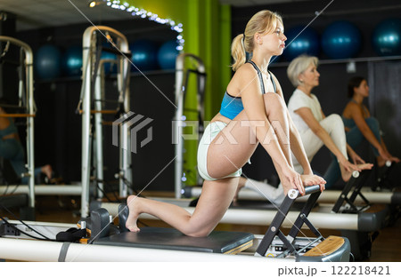 Young woman standing on knee reformer, perform exercises and body tilts. 122218421