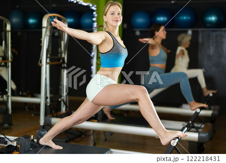 Young woman standing on pilates reformer, perform exercises Young woman standing on pilates reformer, perform exercises 122218431