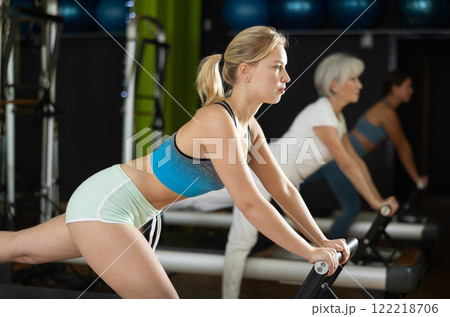 Young woman standing on pilates reformer, perform exercises 122218706