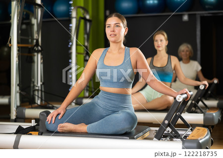 Girl sitting on foldable bed reformer performs exercises, strengthening body and muscles Girl sitting on foldable bed reformer performs exercises, strengthening body and muscles 122218735