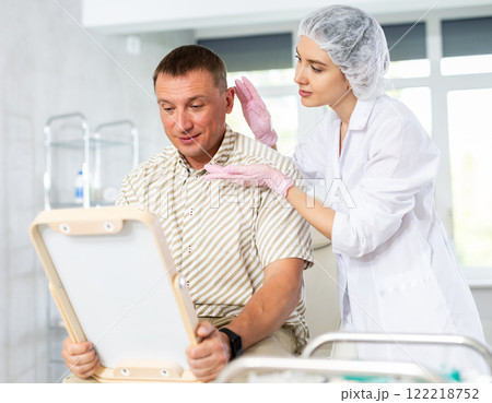 Satisfied middle-aged man patient holding mirror sitting on clinical chair Satisfied middle-aged man patient holding mirror sitting on clinical chair 122218752
