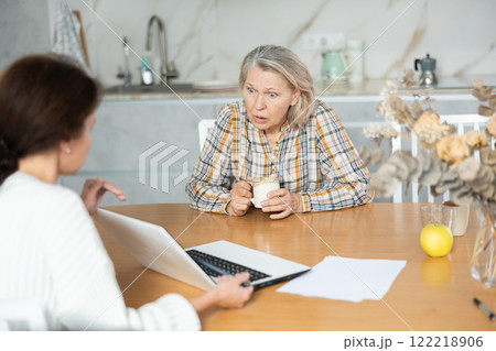 Indignant old woman sitting at the kitchen-table face to face with middle-aged female agent Indignant old woman sitting at the kitchen-table face to face with middle-aged female agent 122218906