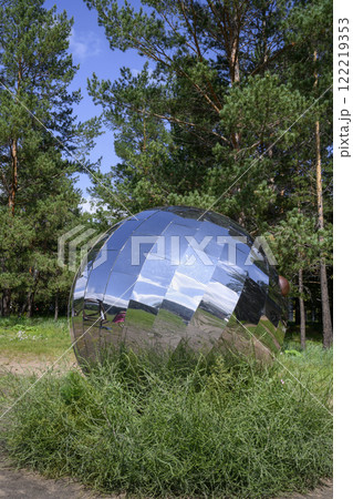A huge mirror ball in the park on the grass among the pines in summer 122219353