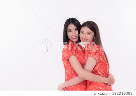 Two women in vibrant red dresses embrace joyfully, showcasing cultural tradition and friendship. Two women in vibrant red dresses embrace joyfully, showcasing cultural tradition and friendship. 122219392