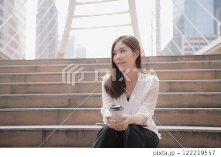 A woman enjoying coffee while sitting on outdoor steps in an urban setting. A woman enjoying coffee while sitting on outdoor steps in an urban setting. 122219557