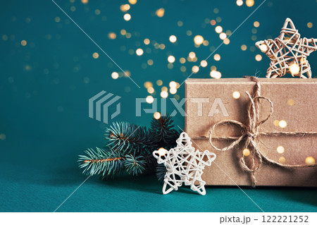Festive gift box with pine branch and stars on teal background with bokeh lights Festive gift box with pine branch and stars on teal background with bokeh lights 122221252