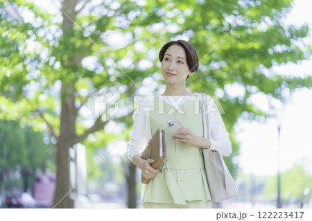 新緑の中、手帳とスマホを手にするビジネスウーマンのポートレート 新緑の中、手帳とスマホを手にするビジネスウーマンのポートレート 122223417