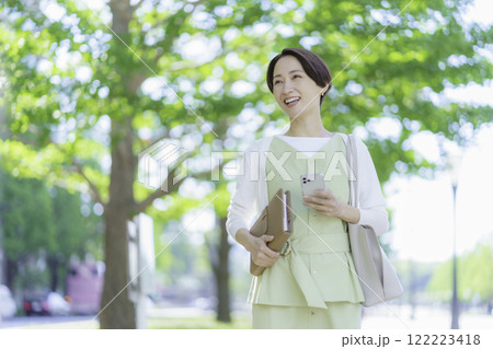新緑の中、手帳とスマホを手にするビジネスウーマンのポートレート 122223418