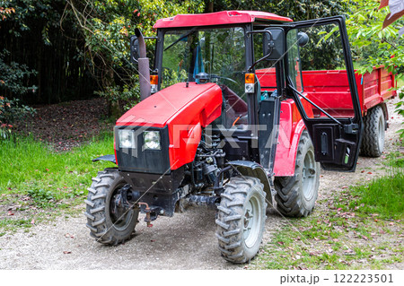 Red wheeled tractor with a trailer on a dirt road in a deciduous forest 122223501