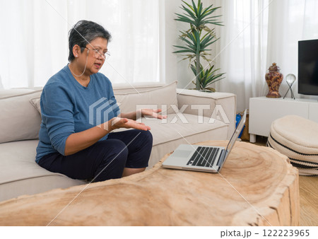 Elderly lady actively engaged with technology at home. She is surrounded by a cozy living room ambiance. 122223965