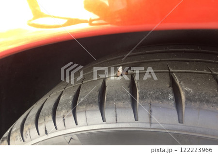 A close-up view show a tire with a nail lodged in its tread, parked in a public lot during sunny weather, raising concern about possible air leakage and safety issue. 122223966