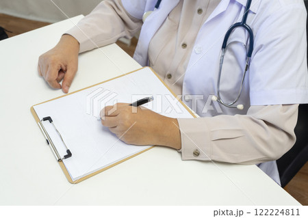 Woman doctor taking notes on clipboard while sitting at her table in office 122224811