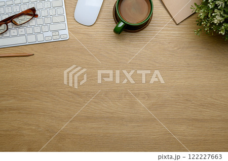 Top view minimalist workspace with keyboard, glasses, cup of coffee and potted plant on wooden table 122227663