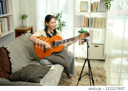 Smiling woman playing acoustic guitar and recording video content for social media with smartphone Smiling woman playing acoustic guitar and recording video content for social media with smartphone 122227687