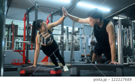 Active couple giving high five each other while doing push up on step platforms in a gym Active couple giving high five each other while doing push up on step platforms in a gym 122227689