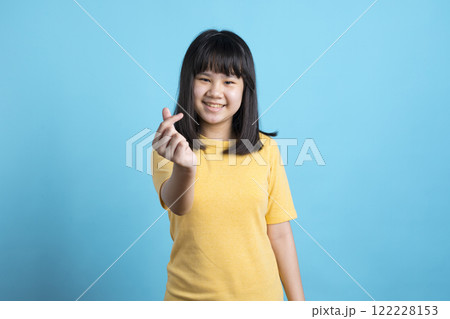 An Asian girl gives a thumbs up and smile on blue background. 122228153