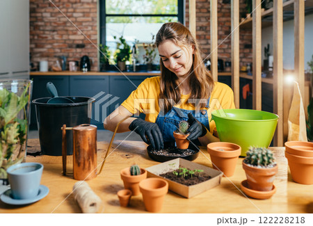 Young woman potting a plant at home. Engaging leisure activities. Indoor gardening. Home planting on the kitchen. Free time for little house gardening concept. Young woman potting a plant at home. Engaging leisure activities. Indoor gardening. Home planting on the kitchen. Free time for little house gardening concept. 122228218