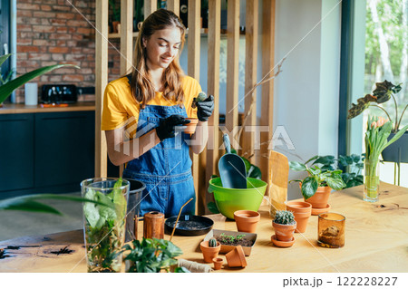 Pretty female wearing overalls gardening at home. Home planting on the kitchen. Free time for little house gardening concept. Pretty female wearing overalls gardening at home. Home planting on the kitchen. Free time for little house gardening concept. 122228227