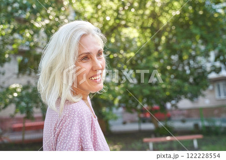 Caucasian mature female smiling outdoors with trees in background on a sunny day 122228554
