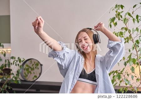 Young caucasian female dancing happily with headphones in cozy indoor setting 122228686