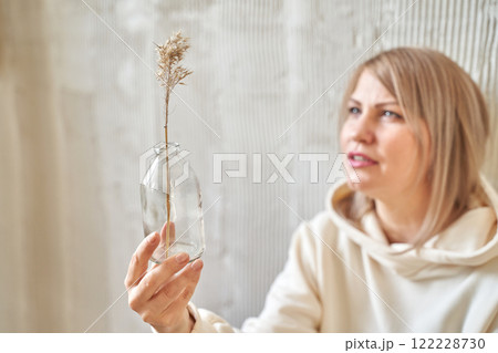 Caucasian female adult holding glass bottle with dried plant, contemplating Caucasian female adult holding glass bottle with dried plant, contemplating 122228730