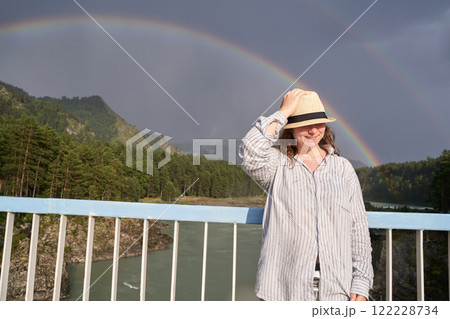 Caucasian young woman wearing a hat on a bridge with a scenic rainbow 122228734