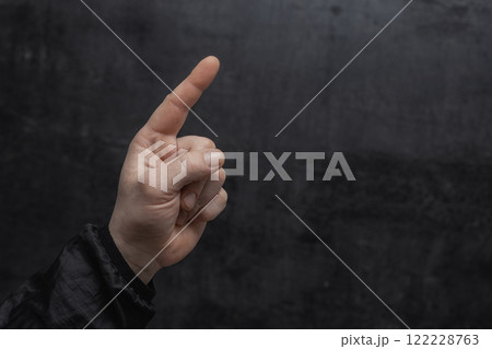 Concept of pointing finger. Close-up of a man in a sweater pointing his finger forward against on dark background. Concept of pointing finger. Close-up of a man in a sweater pointing his finger forward against on dark background. 122228763