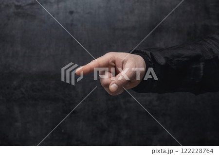 Concept of pointing finger. Close-up of a man in a sweater pointing his finger forward against on dark background. Concept of pointing finger. Close-up of a man in a sweater pointing his finger forward against on dark background. 122228764