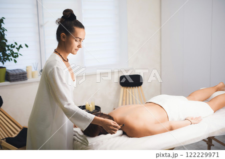 Massage therapist using Palo Santo stick at work with client who lying face down in salon, close-up, selective focus. Massage therapist using Palo Santo stick at work with client who lying face down in salon, close-up, selective focus. 122229971