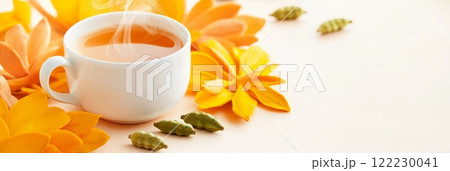 A high-resolution image of a steaming tea cup placed on a light background, surrounded by bright orange flowers 122230041