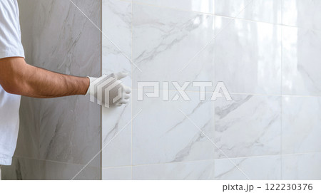 A master tiler checks the quality of laying ceramic tiles on a wall, finishing work on bathroom renovation A master tiler checks the quality of laying ceramic tiles on a wall, finishing work on bathroom renovation 122230376