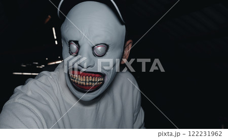 A man in a scary mask and white sweatshirt in a dimly lit attic with light coming through cracks in the background. Attic Monster. A man in a scary mask and white sweatshirt in a dimly lit attic with light coming through cracks in the background. Attic Monster. 122231962