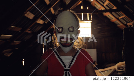 A girl wearing a creepy mask stands in a dimly lit attic with wooden beams and a window in the background. The child is a monster. 122231964