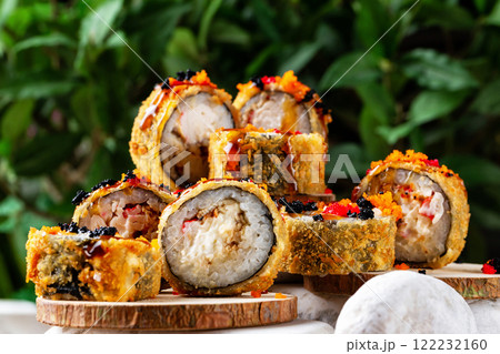 Closeup set of hot tempura sushi rolls with eel, cheese, crab and caviar at small wooden boards on stones at decorated green background. Closeup set of hot tempura sushi rolls with eel, cheese, crab and caviar at small wooden boards on stones at decorated green background. 122232160